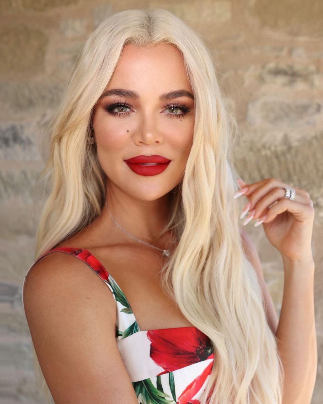 Khloé Kardashian looking at the camera with long blonde hair, red lipstick, and a floral dress.