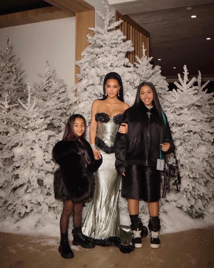 Kim Kardashian and two girls stand in front of frosted Christmas trees.