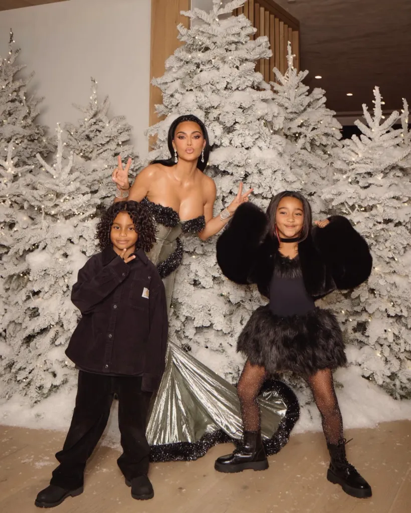 Kim Kardashian posing with her two children in front of snow-dusted Christmas trees.