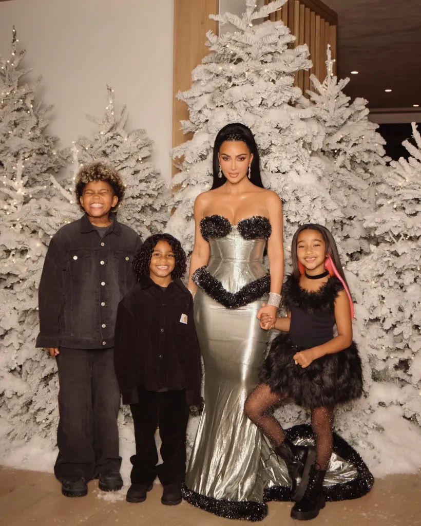 Kim Kardashian and her children in front of snow-covered Christmas trees.