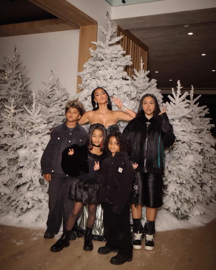 Kim Kardashian and four children posing in front of frosted Christmas trees.