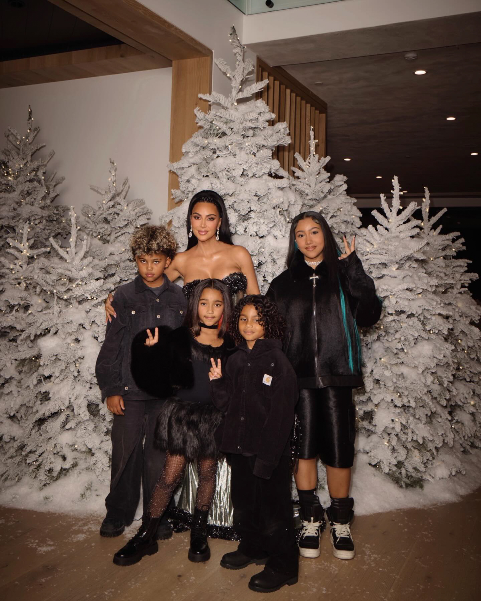 Kim Kardashian with four children posing in front of frosted Christmas trees.