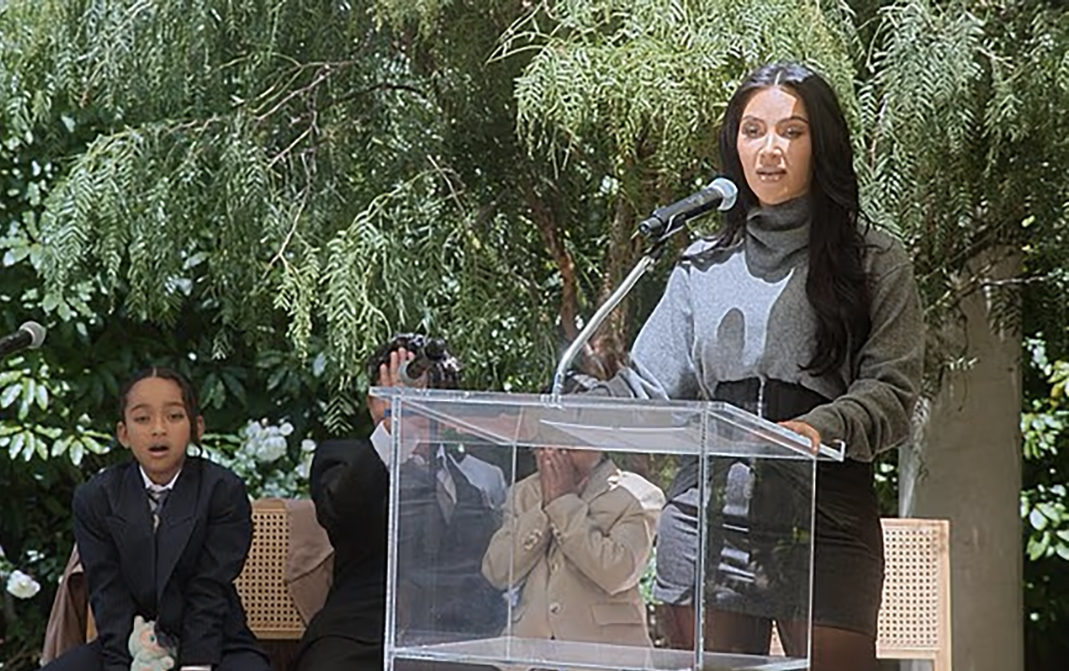 Kim Kardashian speaks at a podium as her sons fight behind her during her law school graduation party.