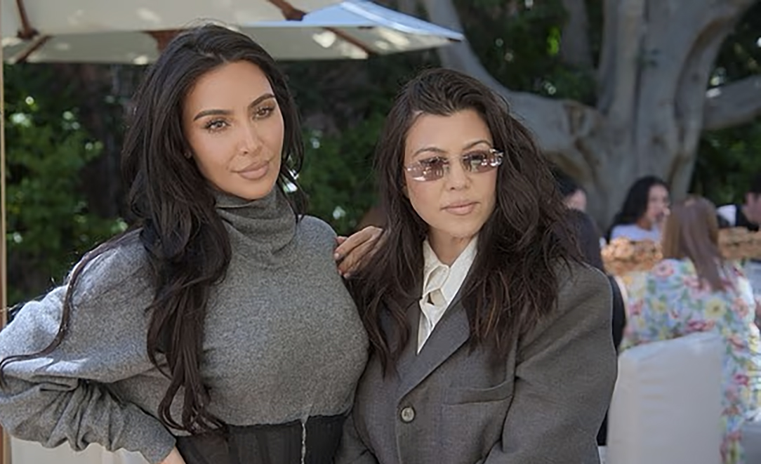 Kim Kardashian in a gray top and Kourtney Kardashian in a gray suit and sunglasses.