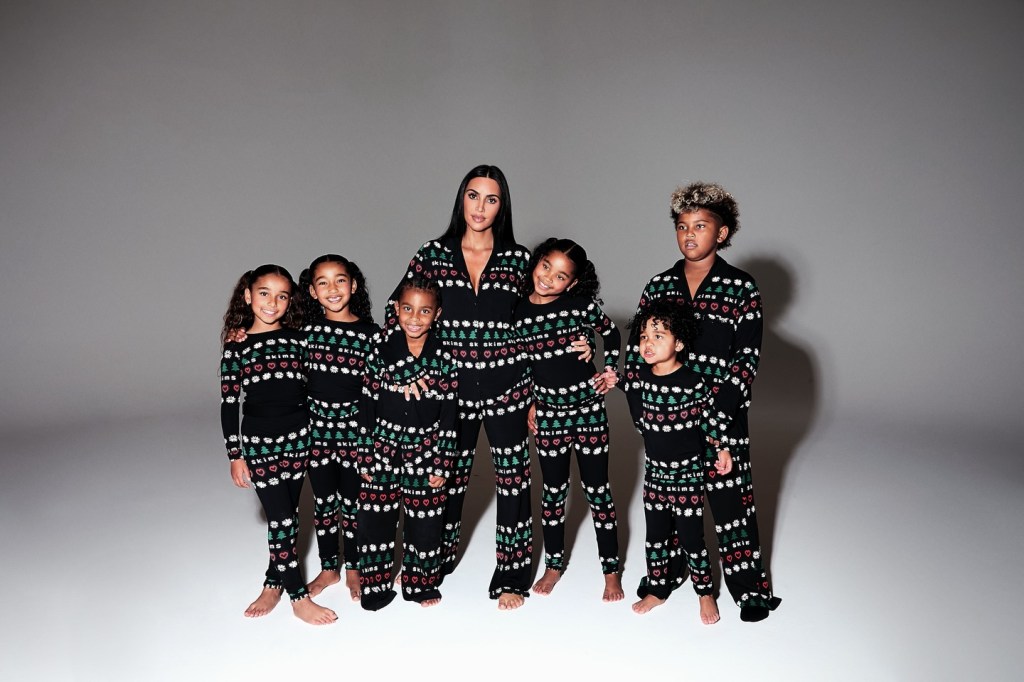 Kim Kardashian and six children wearing matching black pajamas with Christmas trees and hearts.