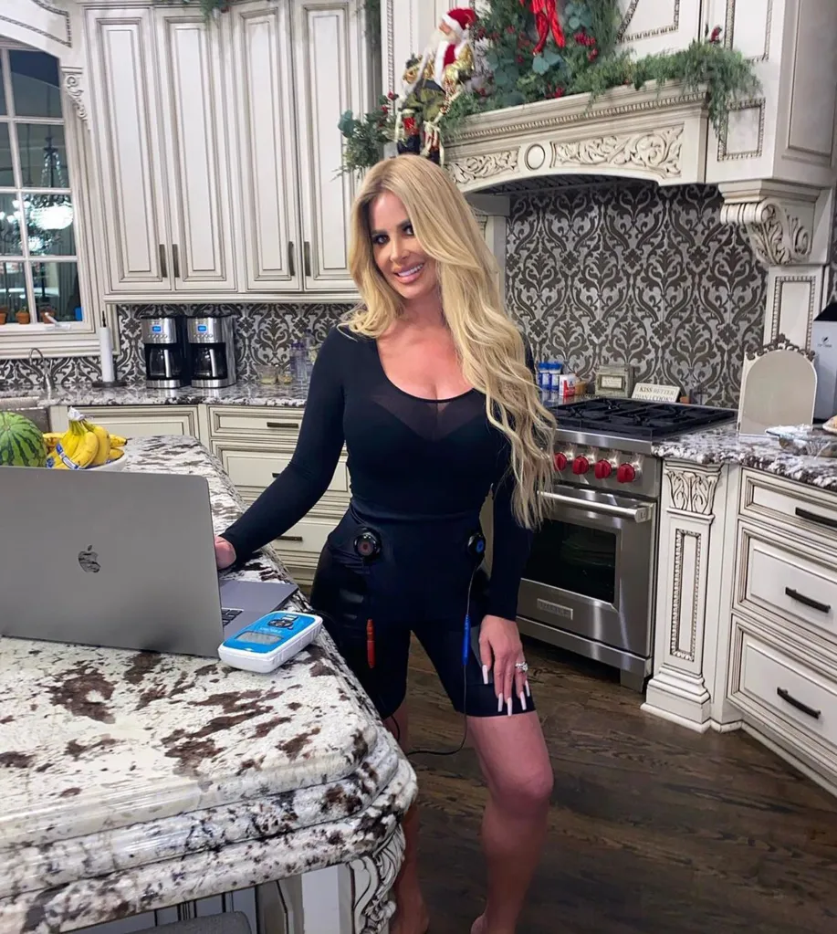 Kim Zolciak in a black long-sleeved top and cycling shorts in a kitchen.