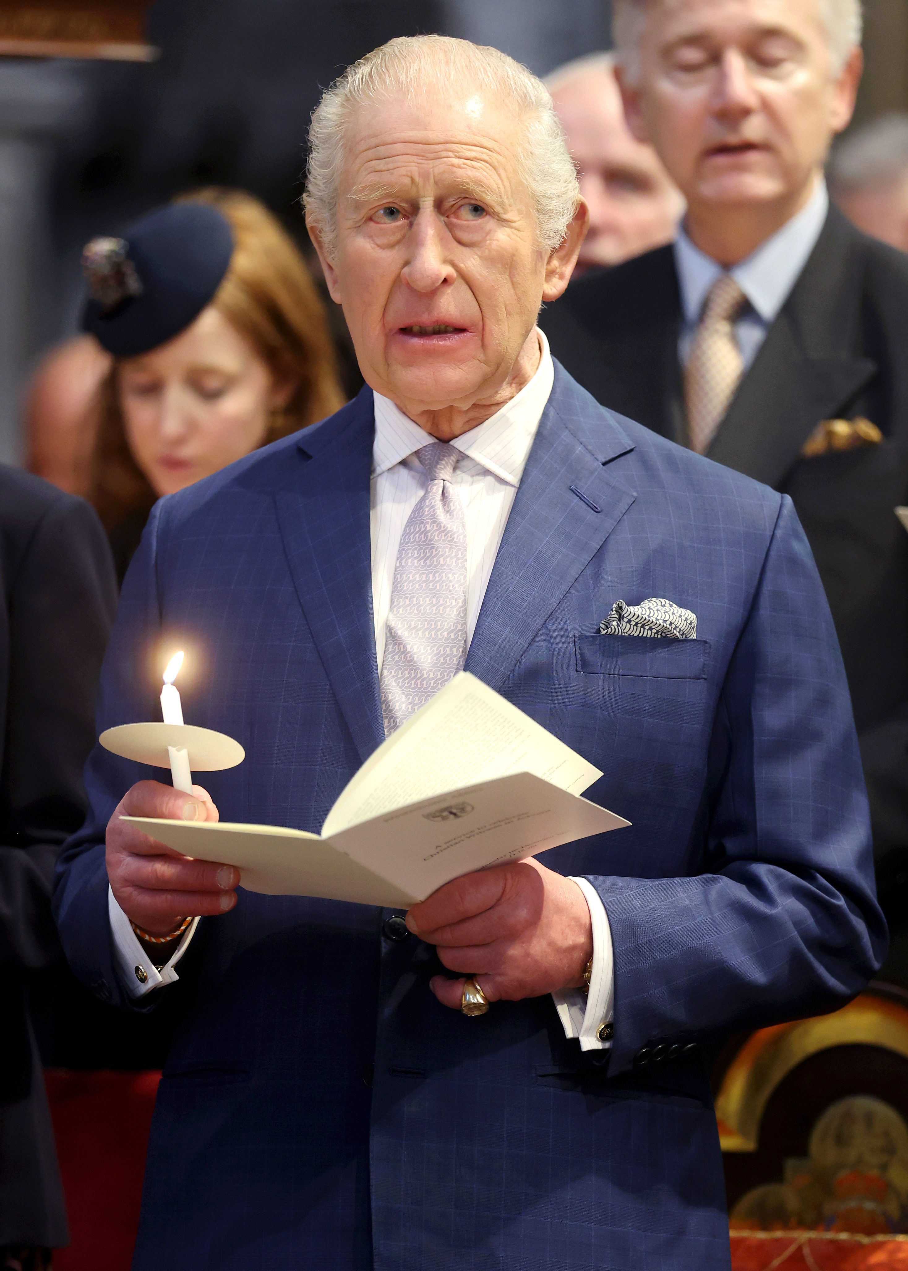 King Charles III holding a lit candle and a program at Westminster Abbey.