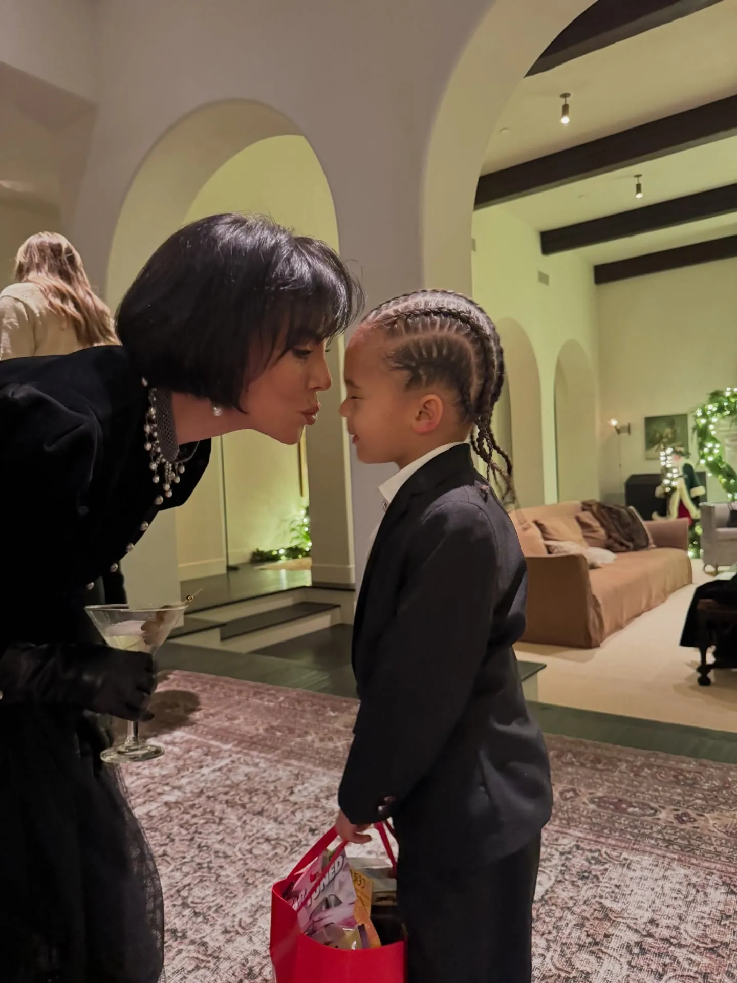 Kris Jenner puckering her lips towards a child in a suit.