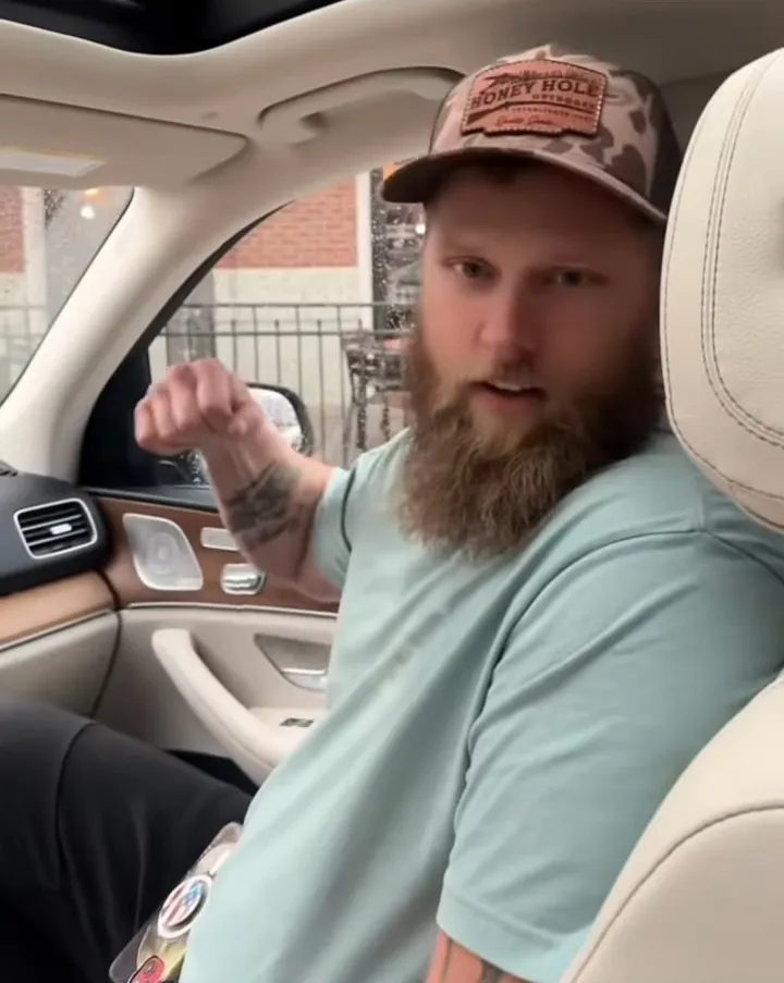 Kyle Chrisley in a car with a baseball cap and beard, looking towards the viewer.