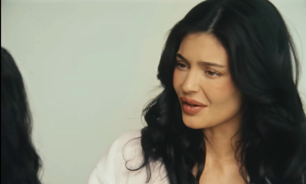 Kylie Jenner with dark hair, looking down and to her right, wearing a light-colored sweater.