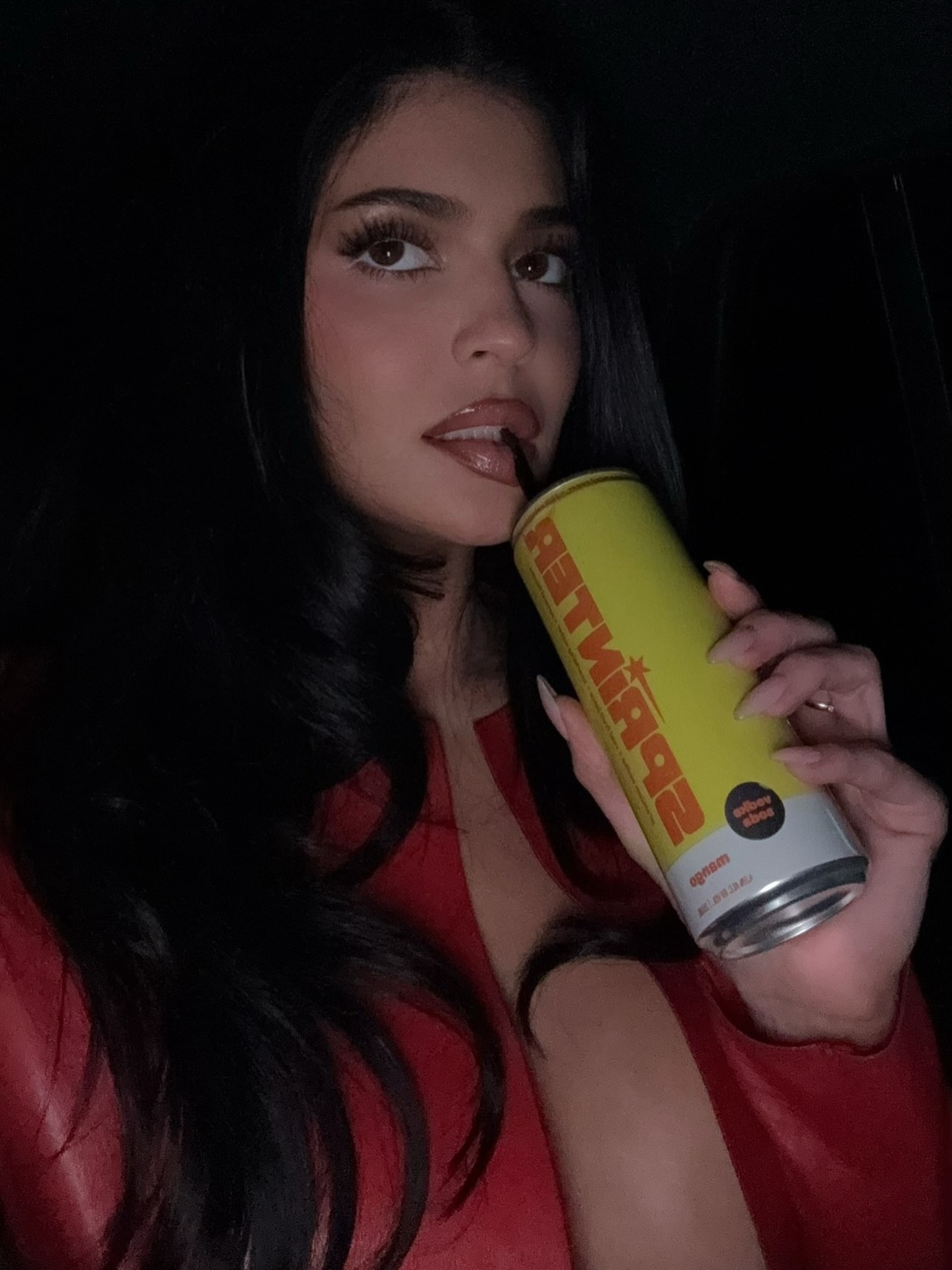 Kylie Jenner in a red plunging top, holding a yellow Sprinter can to her lips.