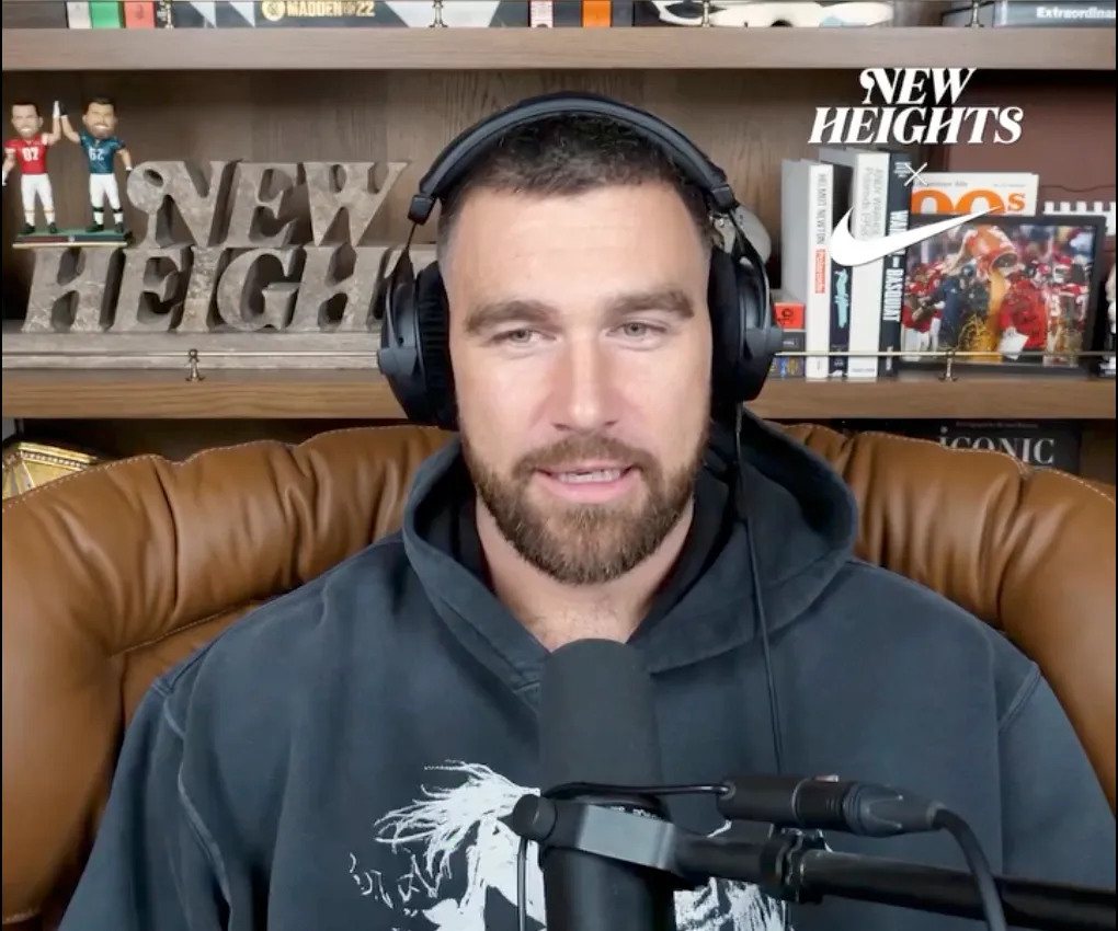 Jason Kelce wearing headphones and a hoodie in front of a 