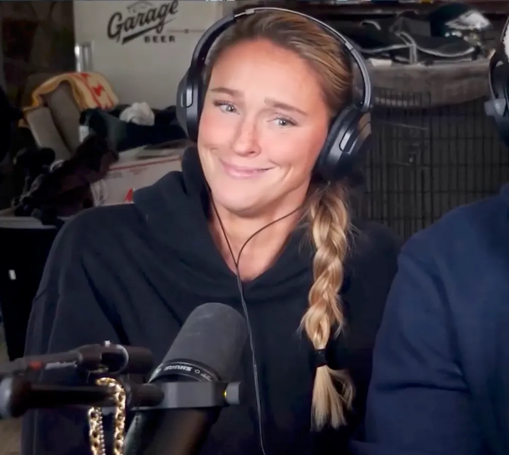 Kylie Kelce smiling while wearing headphones and a black hoodie, with a microphone in front of her.