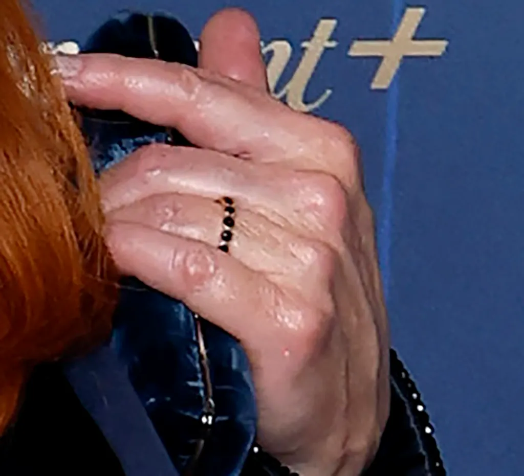Reba McEntire's hand with a black beaded ring, with Rex Linn's hand in the background.