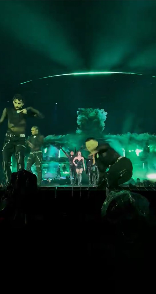 Lady Gaga performing in a green-lit concert with dancers.