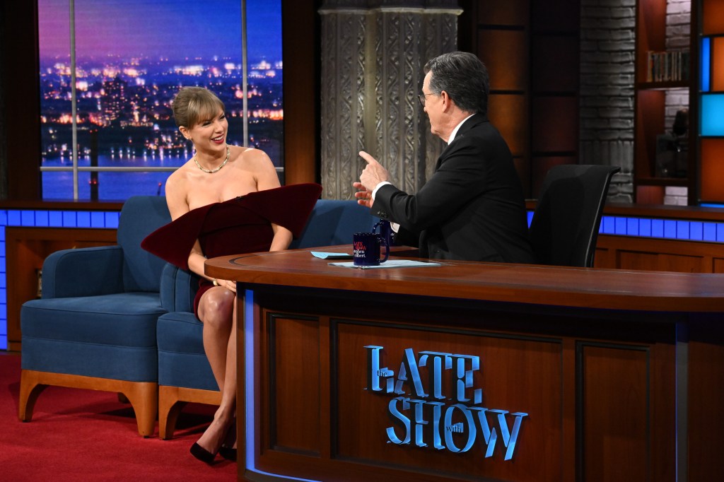 Taylor Swift seated on a blue couch across from Stephen Colbert at a desk on The Late Show.