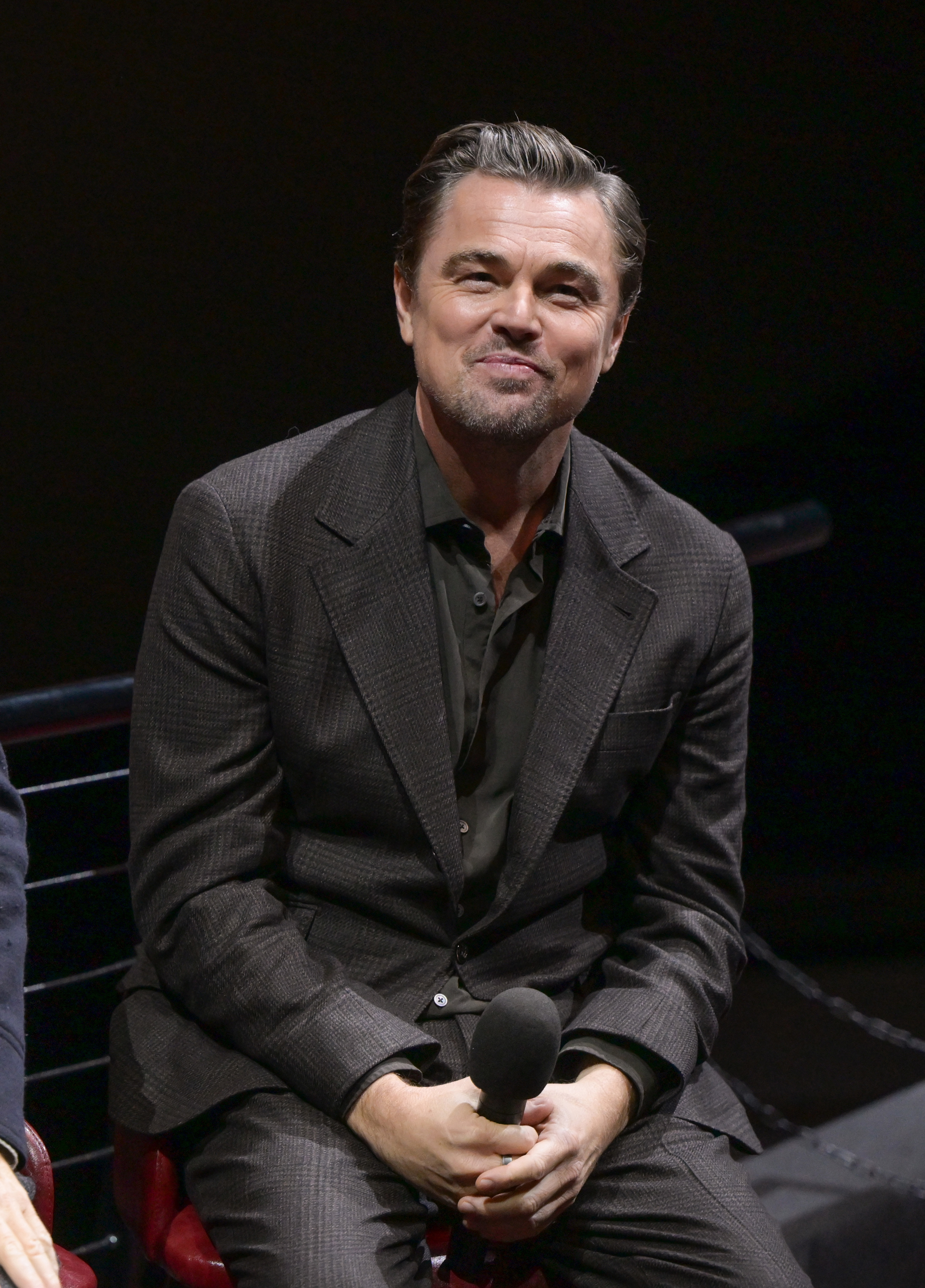 Leonardo DiCaprio smiling while seated, holding a microphone.