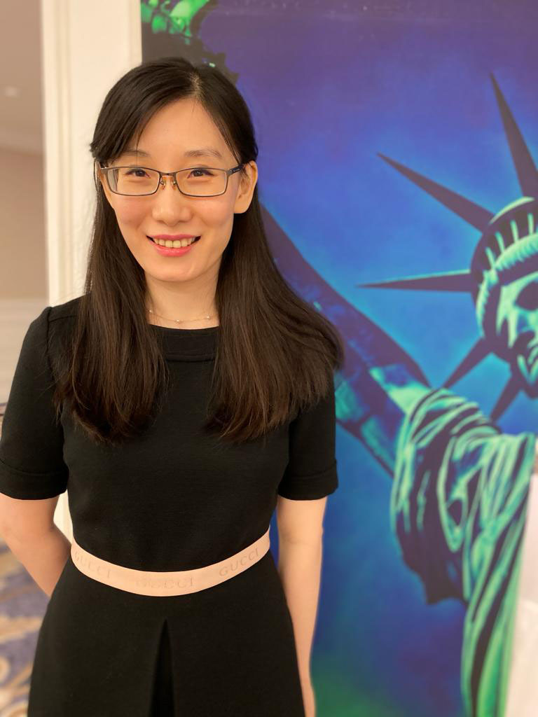Li-Meng Yan, a Chinese virologist and whistleblower, smiles in front of a blue banner depicting the Statue of Liberty.