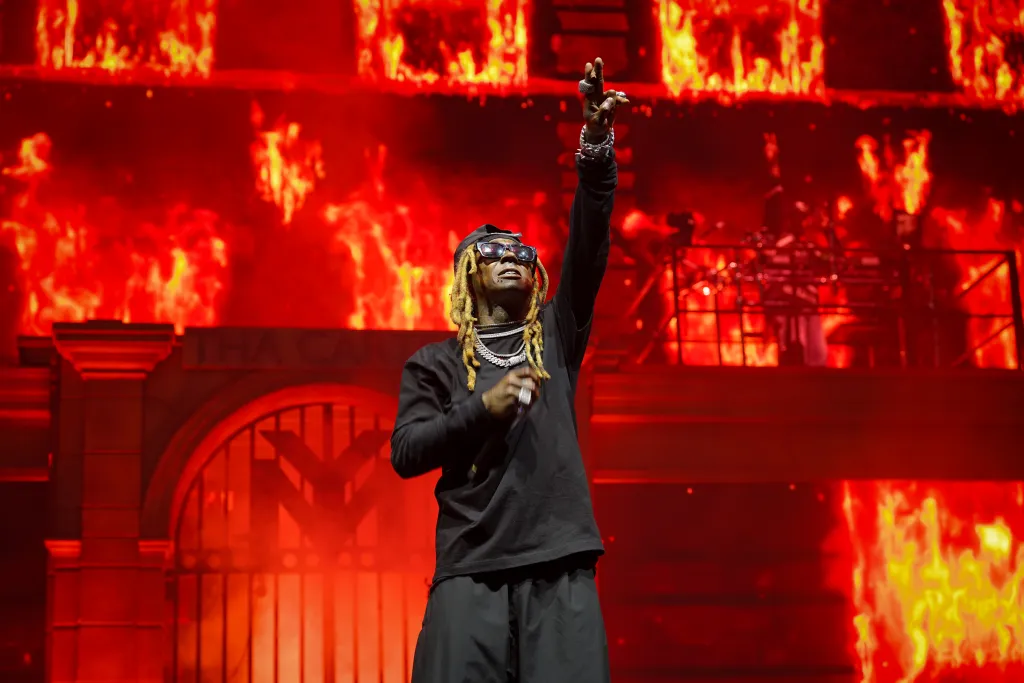 Lil Wayne performing onstage with fire effects in the background.
