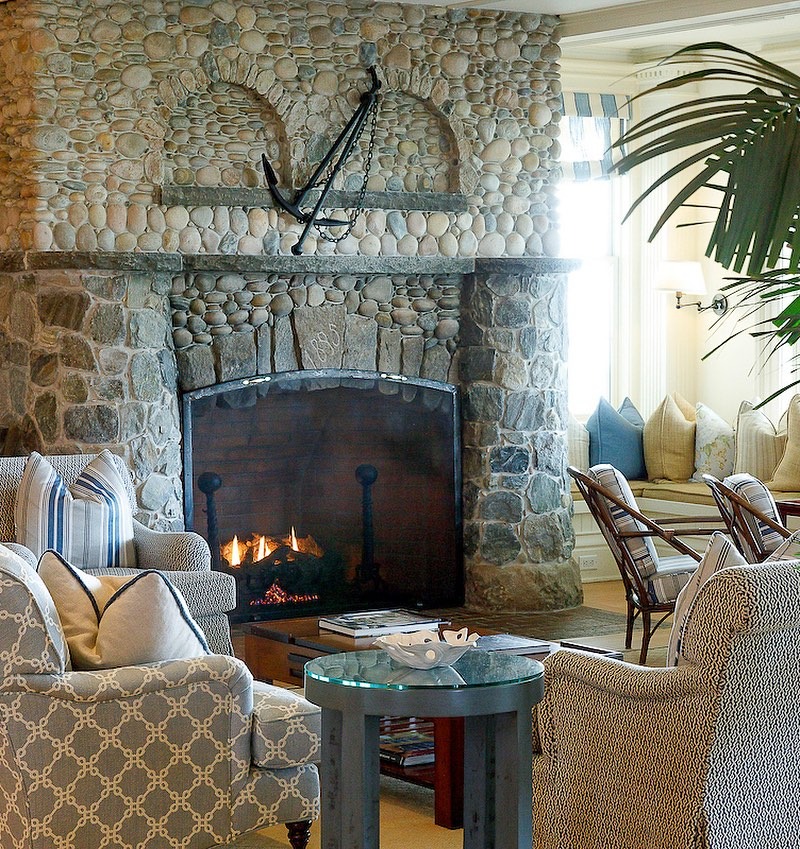 A cozy hotel lobby with a large stone fireplace, lit fire, and an anchor decoration above the mantle.