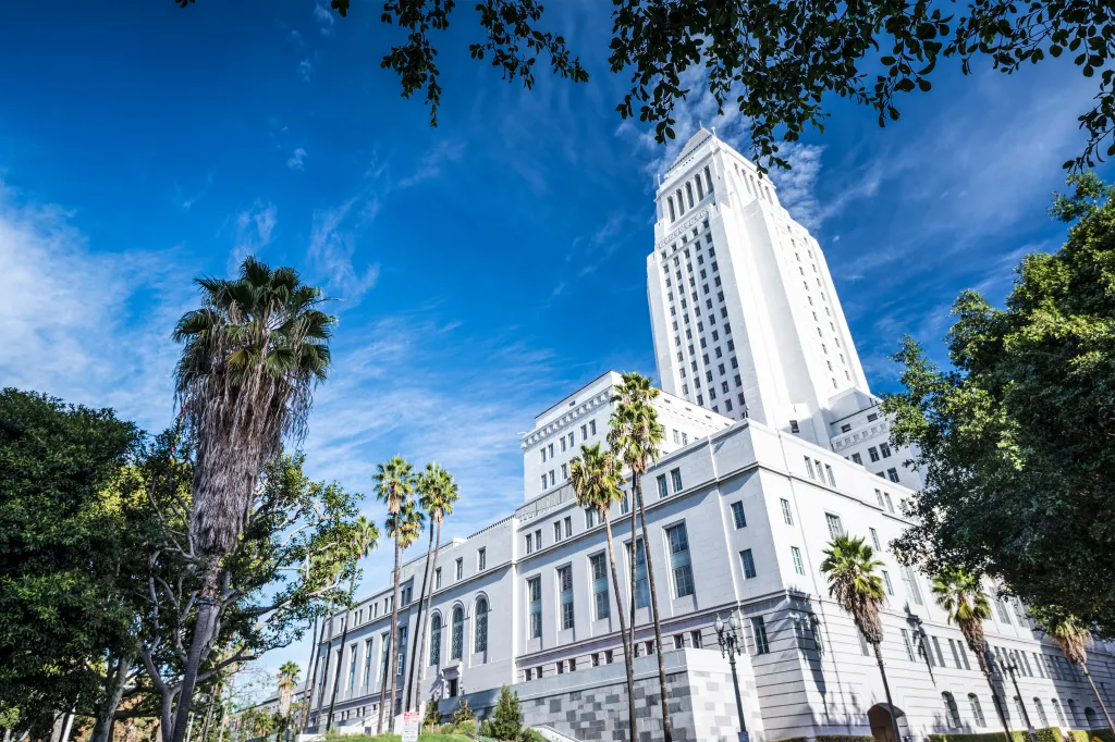 Los Angeles City Hall, an Art Deco skyscraper, stands tall against a bright blue sky with wispy clouds.