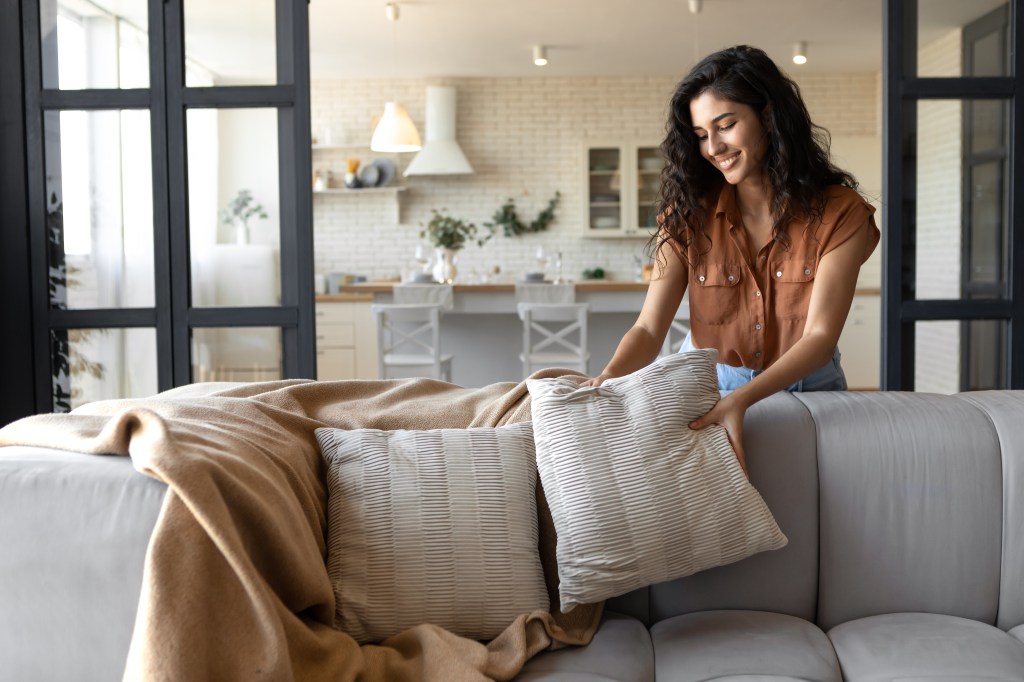 Young woman placing pillows on a couch.