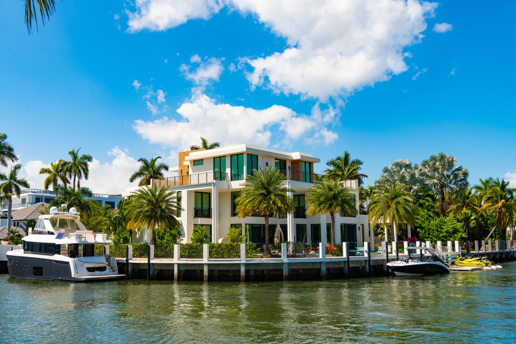Luxury summer villa in Fort Lauderdale, Florida, with a yacht and two jet skis docked at a private pier.