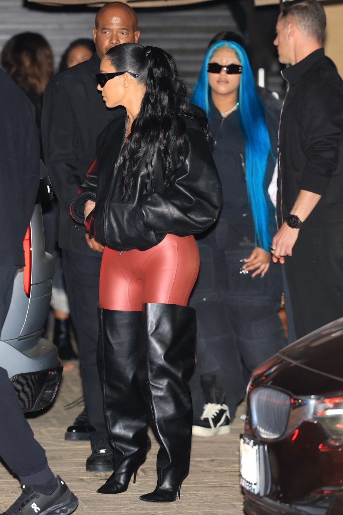Kim Kardashian in a black leather jacket, red pants, and black thigh-high boots, with daughter North West in blue hair.