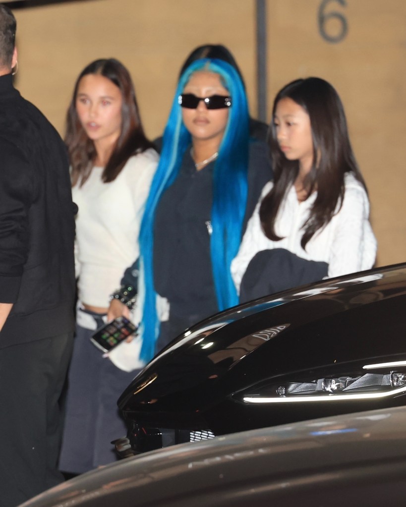 North West with long, bright blue hair and sunglasses, walking with two other young women.
