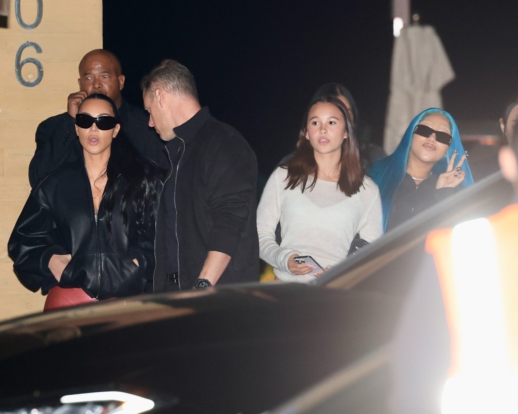 Kim Kardashian in a black leather bomber jacket and red pants with her daughter North West in an all-black oversized outfit and blue hair, dining out with friends.