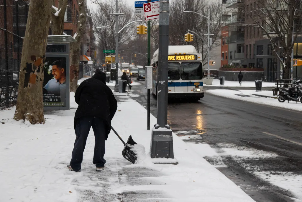 A man shovels snow from a sidewalk in New York City in Dec 2024