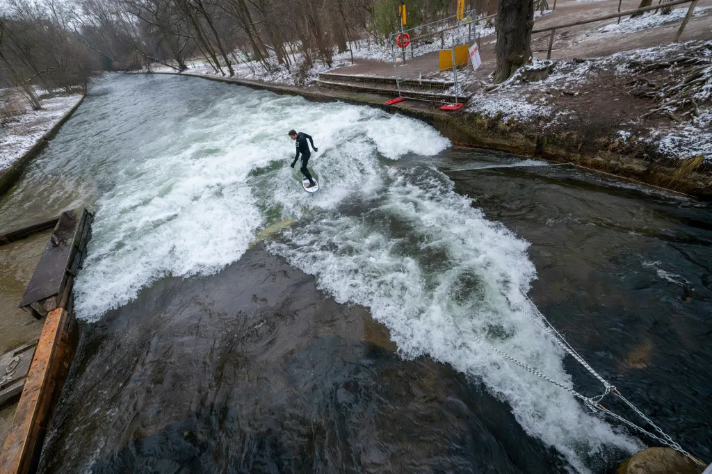 A man in a wetsuit surfs on a standing wave in the Eisbach river.