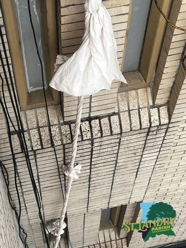 A makeshift rope made of white fabric sheets hanging from a window of a brick building.
