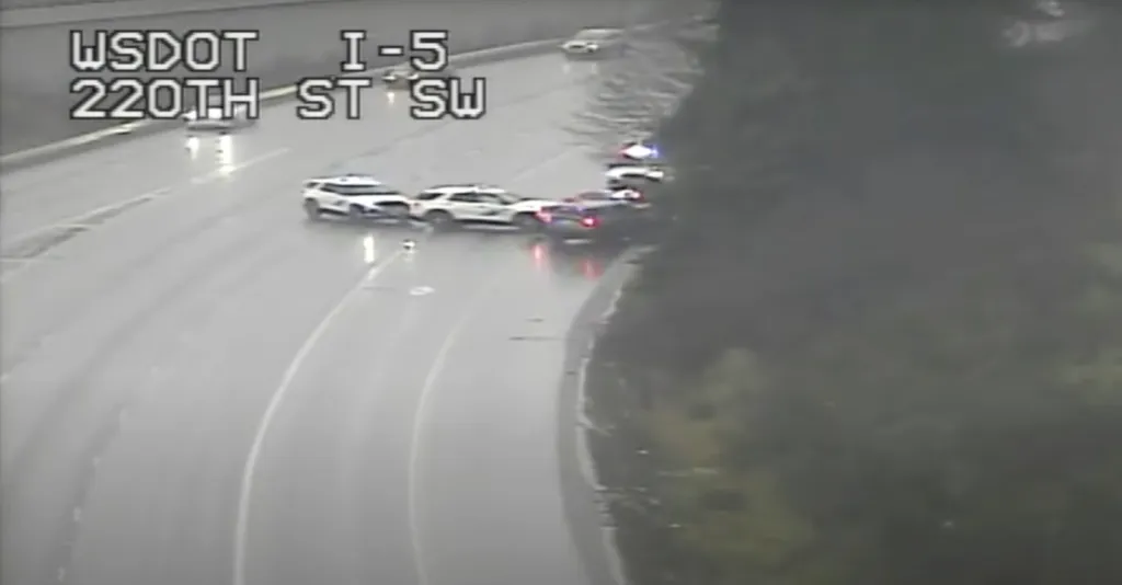 An aerial view of multiple police cars stopping a dark car on a wet highway.