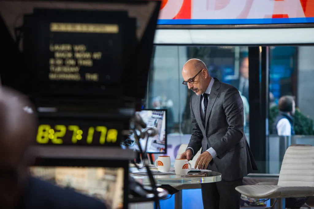 Matt Lauer behind the scenes of his show, bending over a clear glass table with two white mugs.
