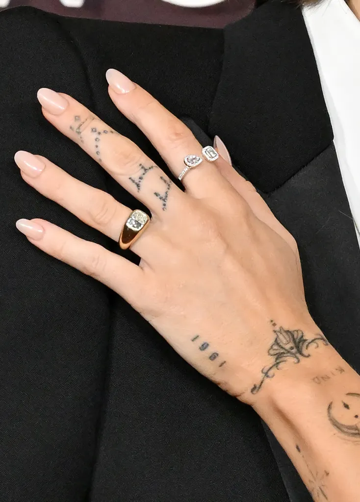 Miley Cyrus's hand with various tattoos and rings.