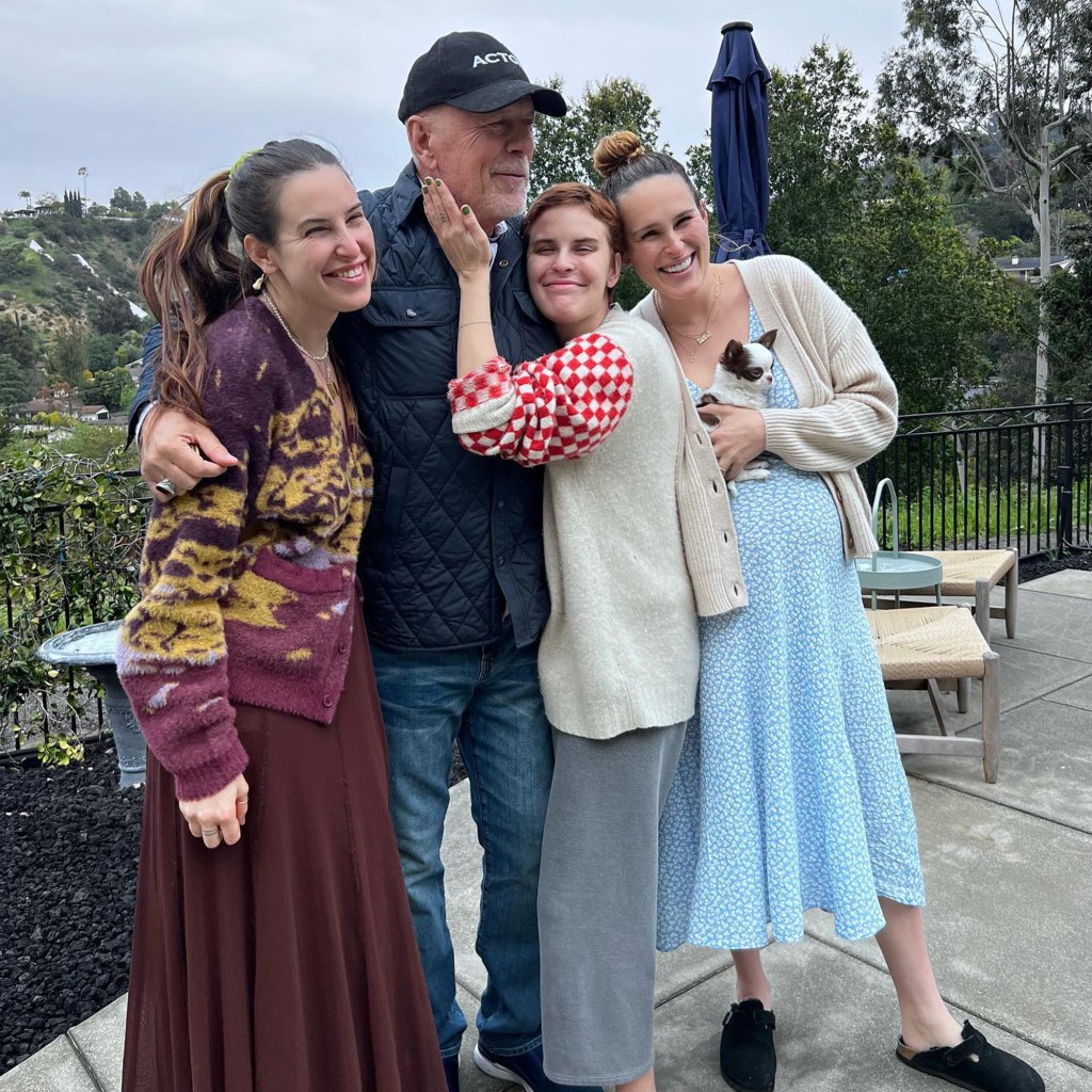 Bruce Willis and three of his daughters smiling outdoors, one holding a small dog.