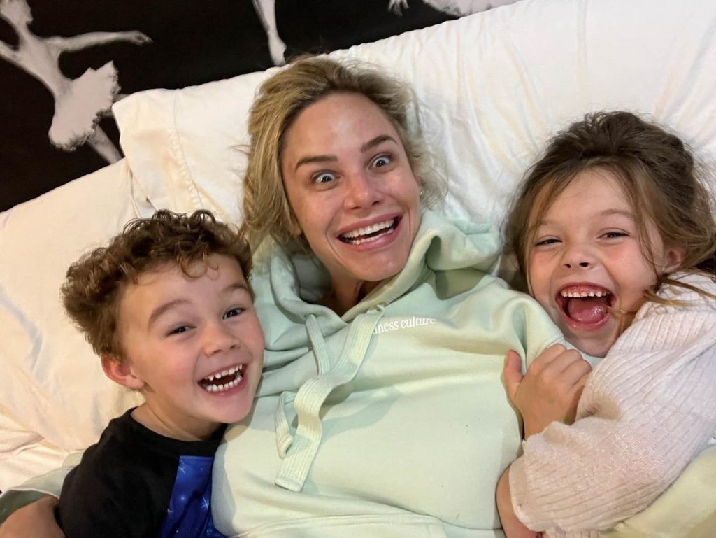 Meghan King with her two kids, all laughing while lying on a bed.