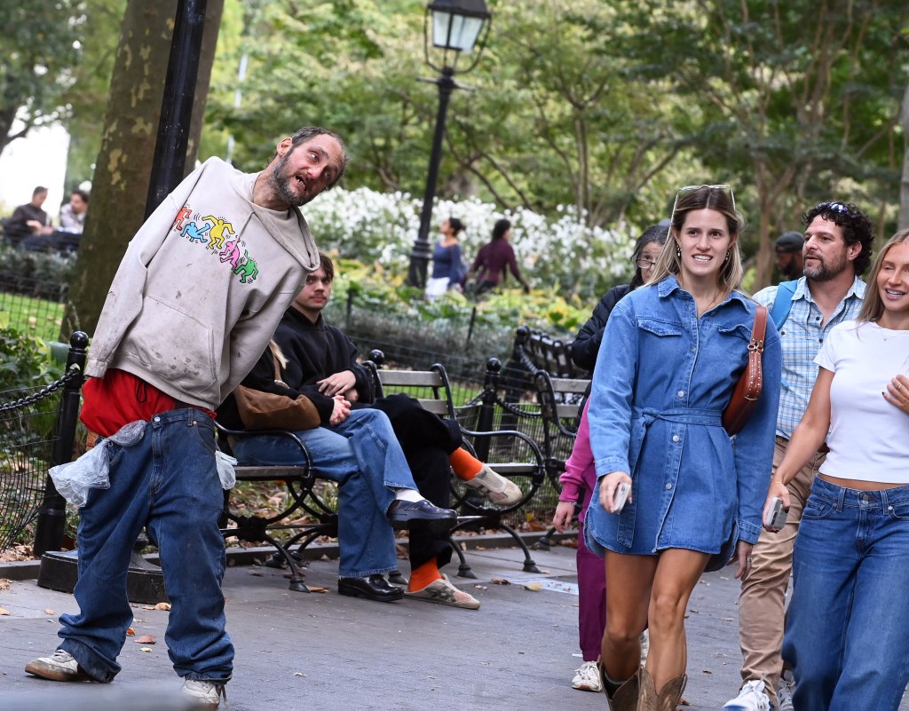 Mentally ill man with pants down in Washington Square Park as people walk by.