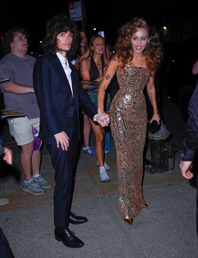 Miley Cyrus and Maxx Morando holding hands as they walk through a crowd.