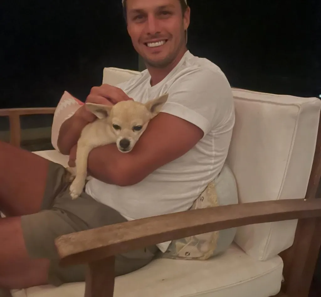 Brendan McLoughlin holding his small dog, Delta, in a white armchair.