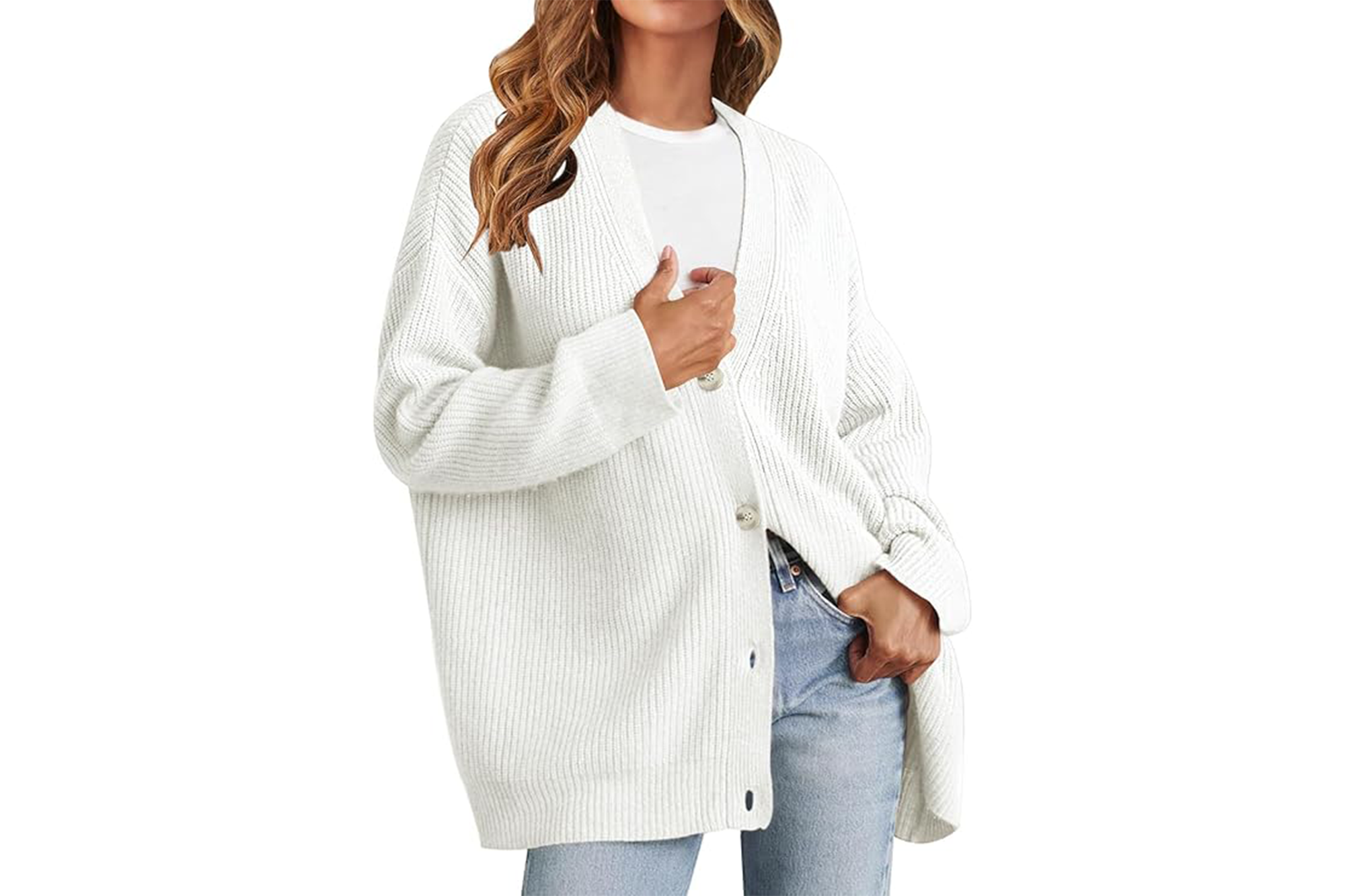 A woman with wavy brown hair models a white oversized cardigan with a white t-shirt and light blue jeans.