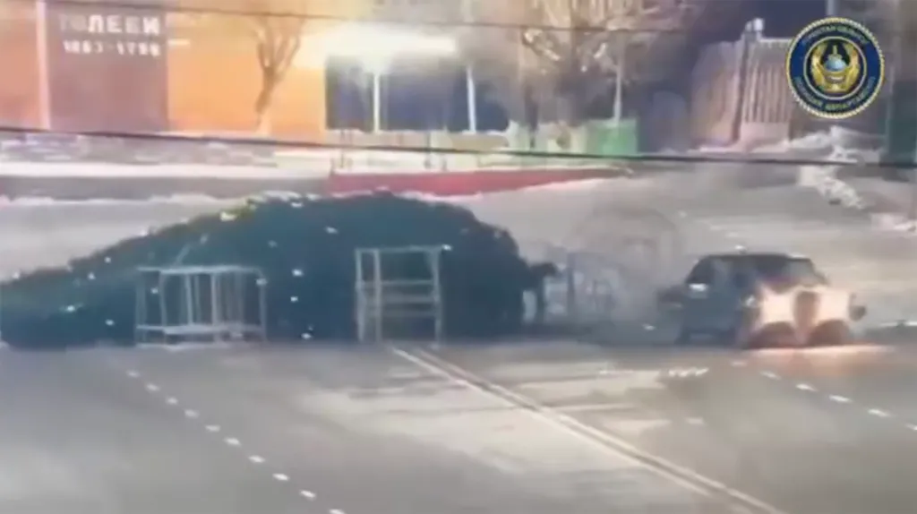A car drifting next to a fallen large Christmas tree at night.