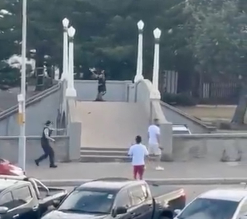 A civilian on a pedestrian bridge kicks away a rifle from an alleged gunman as police and other civilians are nearby.