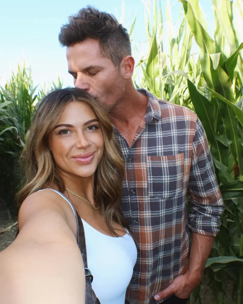 Demi Engemann posing for a selfie while her husband, Bret, kisses her forehead in a cornfield.
