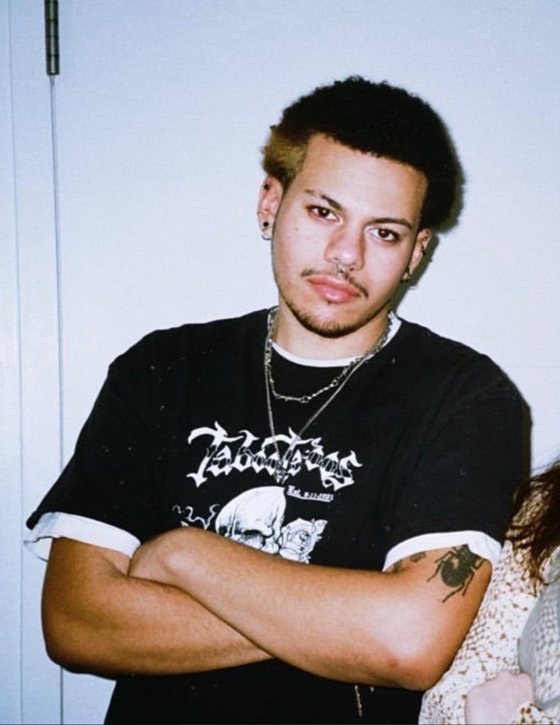 Morty Wortman in a black t-shirt with a white graphic print, multiple piercings, and a beetle tattoo.