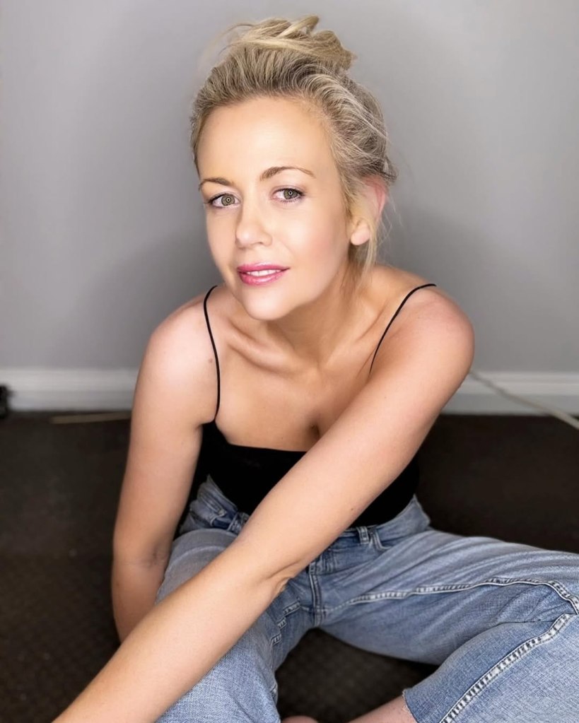 Rachael Carpani sitting on the floor in a black top and jeans.