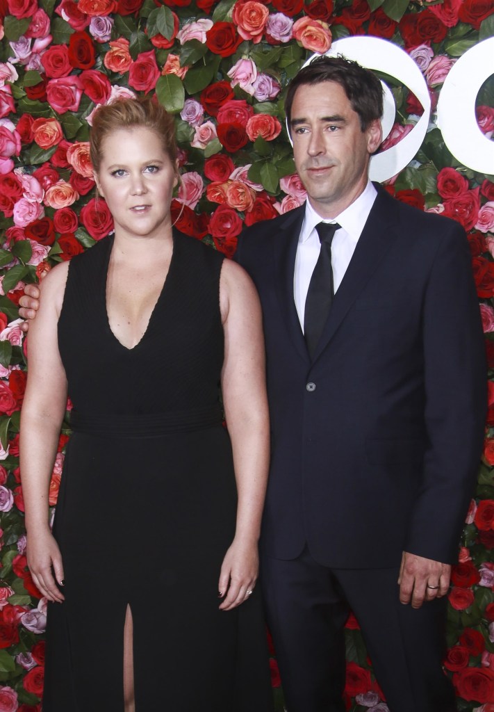 Amy Schumer and Chris Fischer posing together against a backdrop of red and pink roses.