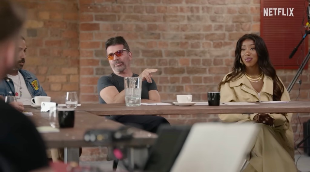 Simon Cowell, in a black T-shirt and black pants, and Kamille in a beige trench coat seen at auditions.