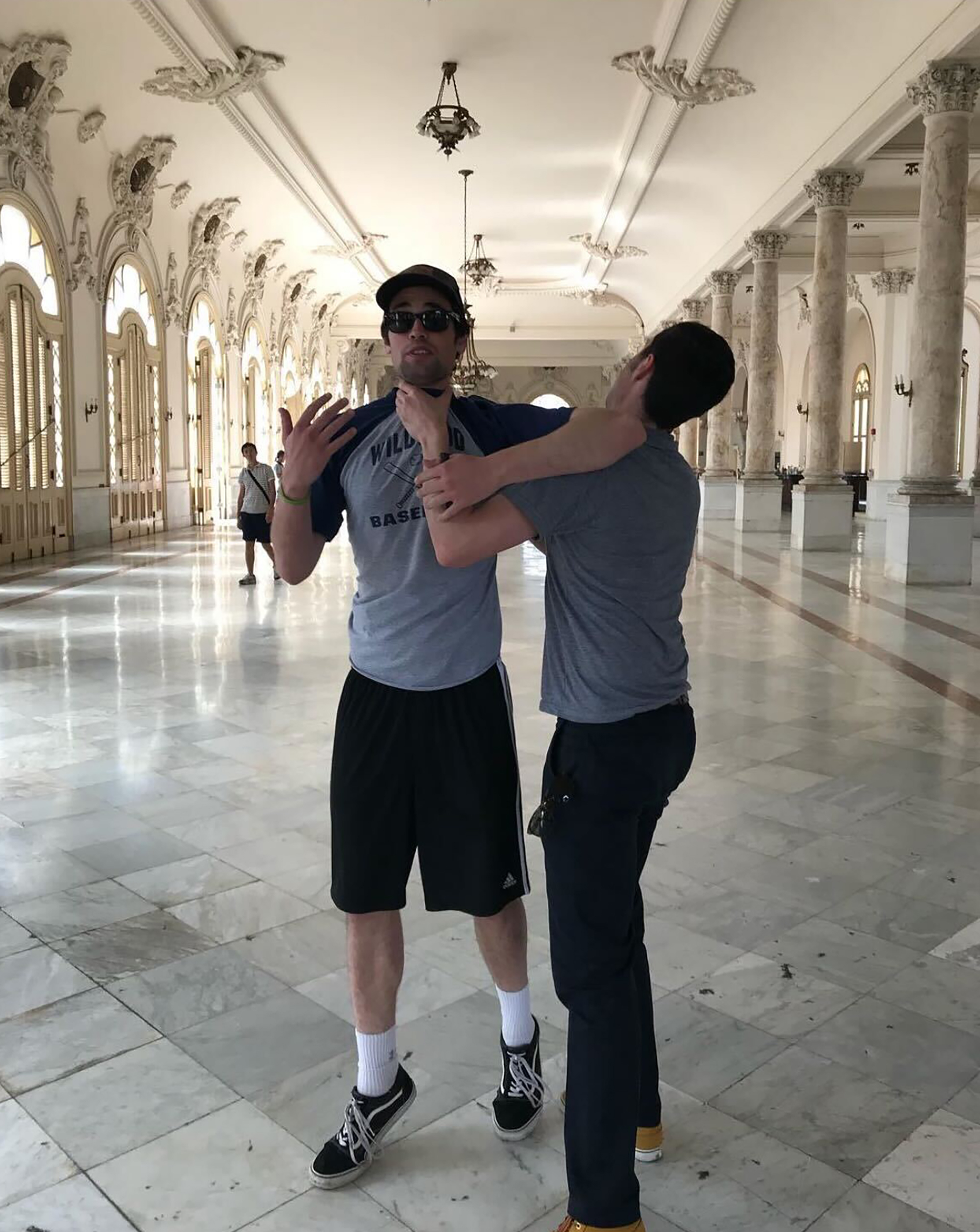 Two men in a grand hall, one grabbing the other by the throat.